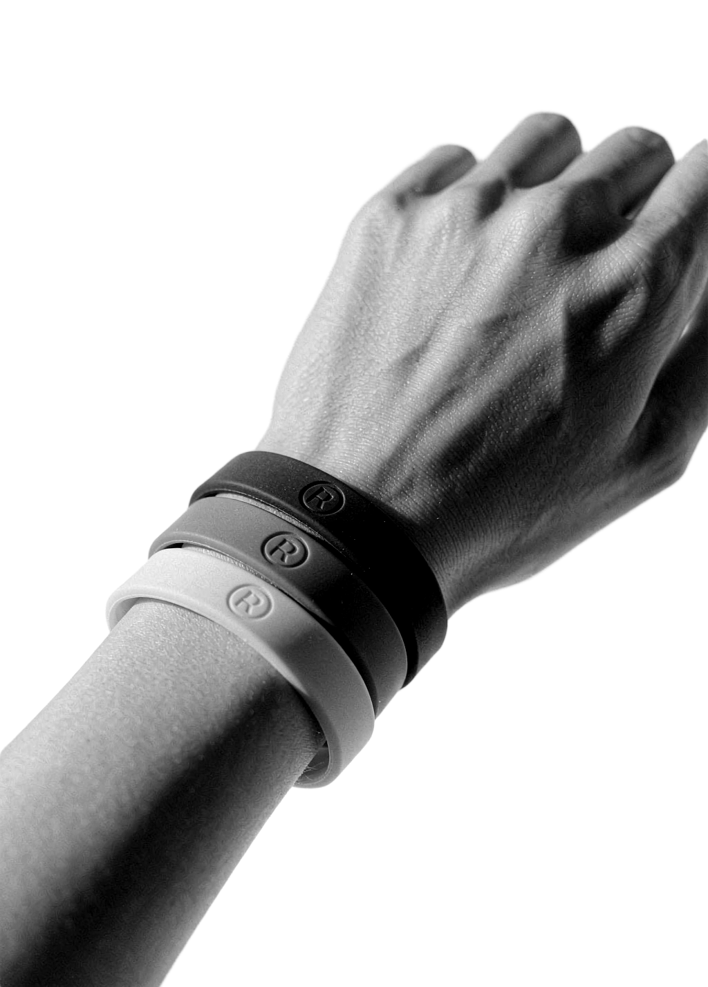 Monochrome studio photo of a wrist stacked with custom silicone wristbands on a white background